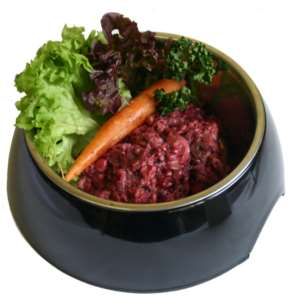 Schwarzer Futternapf, gefüllt mit gewolftem Lamm-Mix. Die Mischung hat eine dunkle, rötlich-braune Farbe und wirkt grob zerkleinert. Die Konsistenz erscheint feucht und fleischig.