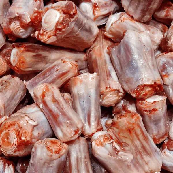 Mehrere Stücke roher Ochsenschwanz mit sichtbaren Knochen und anhaftendem Fleisch. Die walzenförmigen Segmente sind hell bis rötlich gefärbt und weisen teilweise eine leicht glänzende Oberfläche auf.